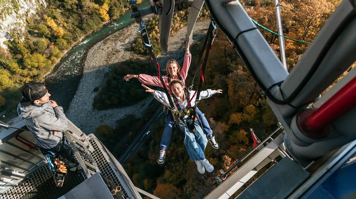 Две подруги раскинули руки на SochiSwing под мостом Skybridge, сверху наблюдает инструктор