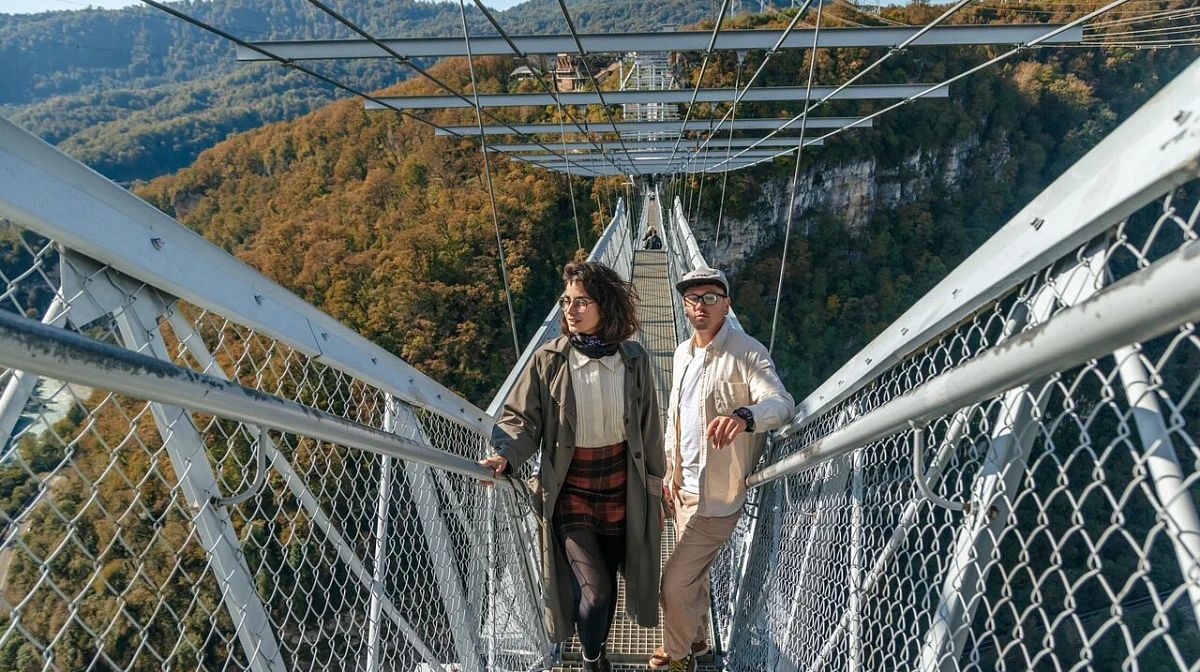 Пара идёт по подвесному мосту Skybridge над осенним лесом Ахштырского ущелья
