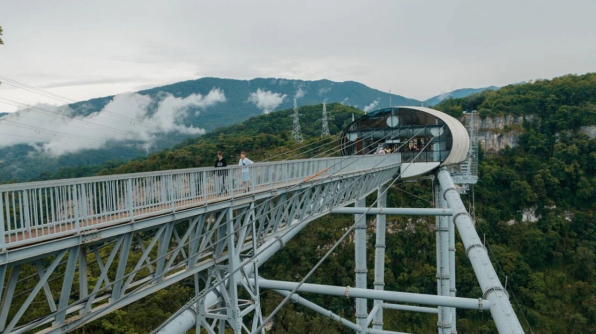 Станция Skybridge с капсулой и пешеходный мост над лесистым ущельем на фоне гор в облаках