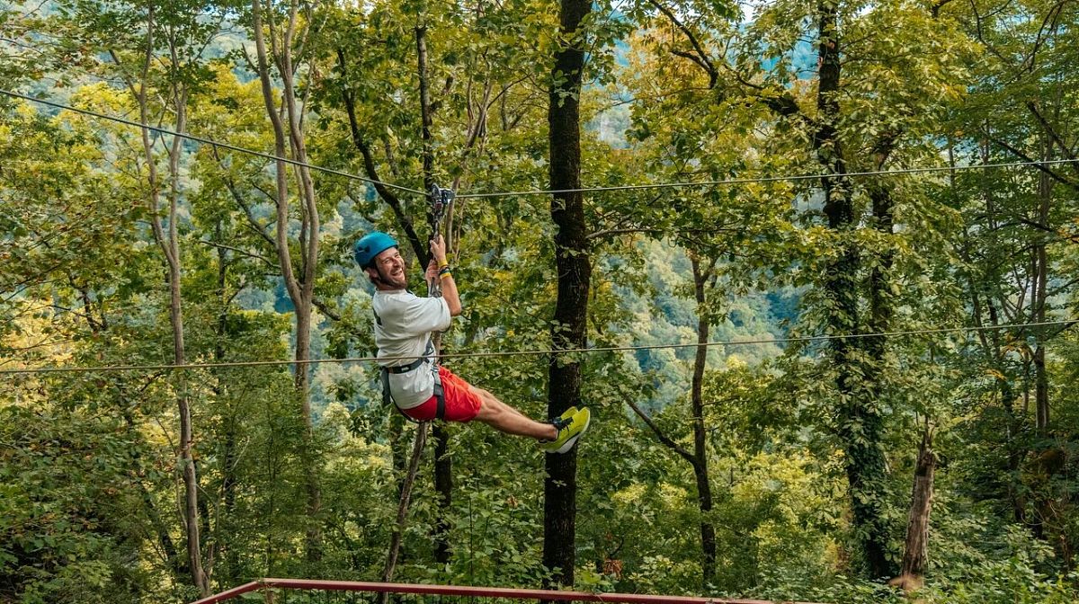 Мужчина в каске скользит по тросу Верёвочного парка Skypark над лесистым склоном