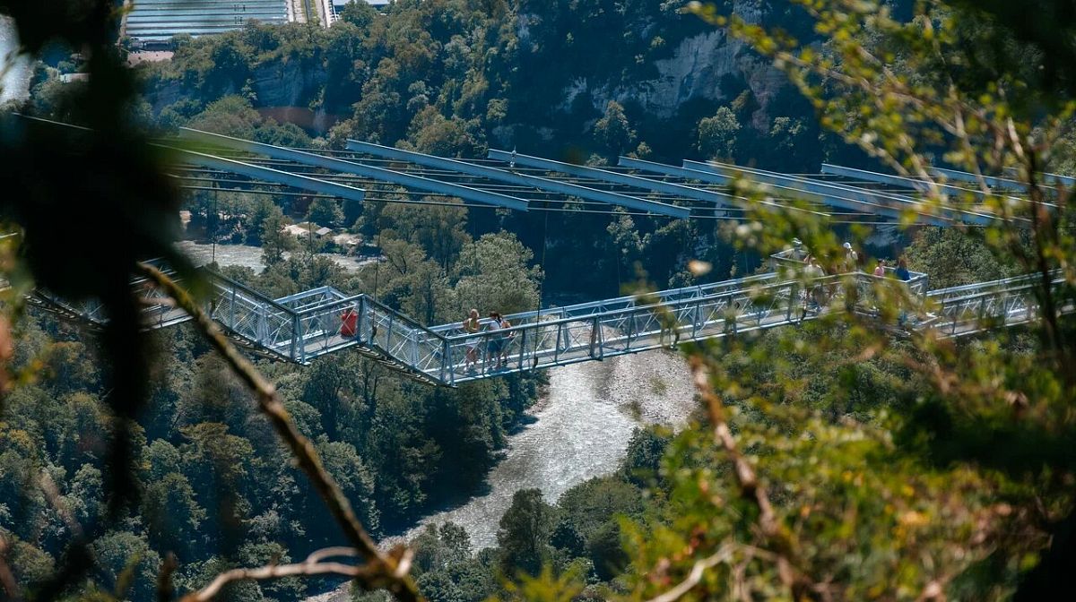 Подвесной мост Skybridge с гуляющими людьми над рекой в Ахштырском ущелье летом