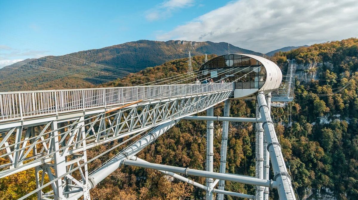Стеклянная капсула и пролёт Skybridge в Скайпарке на фоне осенних гор
