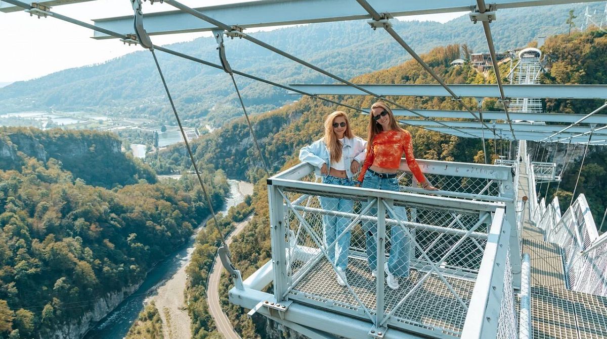 Две девушки на смотровой площадке моста Skybridge над рекой в осеннем Ахштырском ущелье