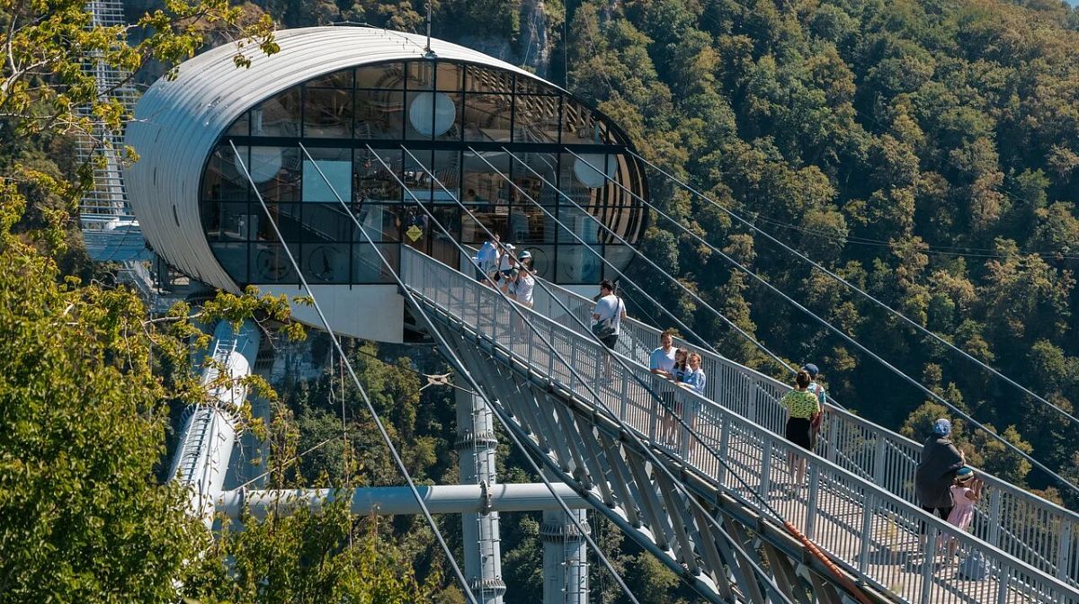Гости идут по мосту Skybridge к станции с овальным остеклением над лесистым ущельем