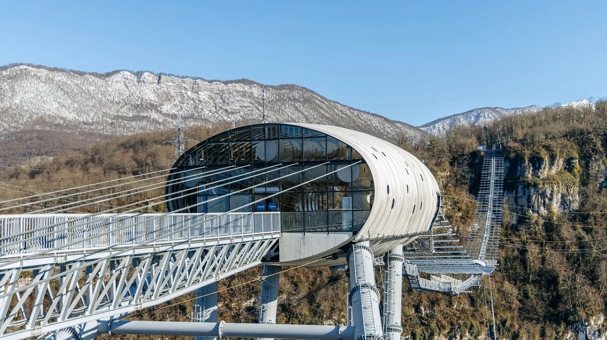 Панорамная капсула моста Skybridge в Скайпарке на фоне заснеженных гор под ясным небом