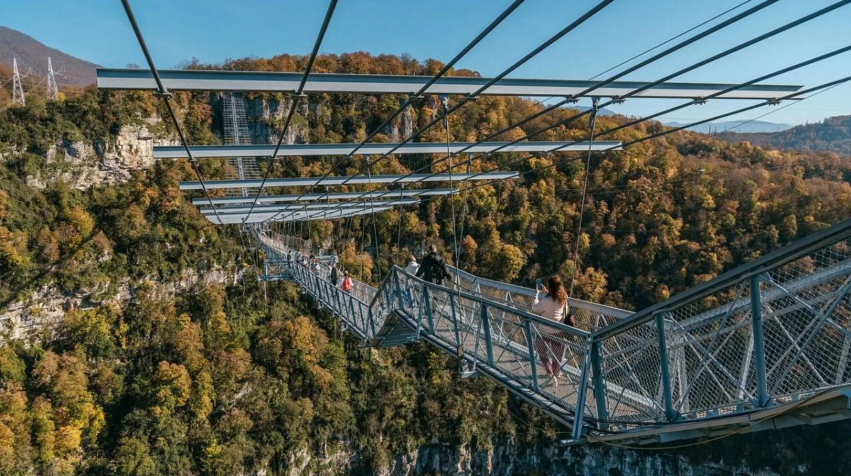 Гости на подвесном мосту Skybridge над осенним лесом и скалами Ахштырского ущелья