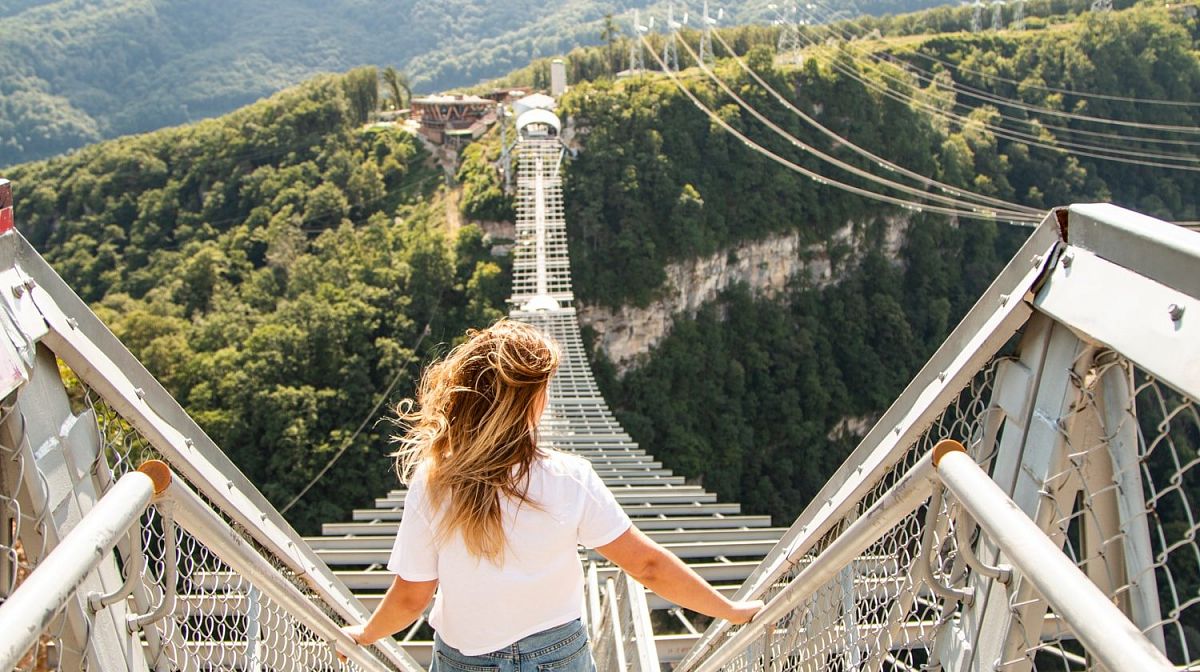 Девушка со спины стоит у начала моста Skybridge и смотрит вдоль настила над ущельем